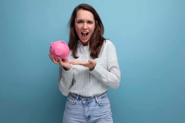 Smiling attractive european brunette young lady keeps money in a pink piggy bank