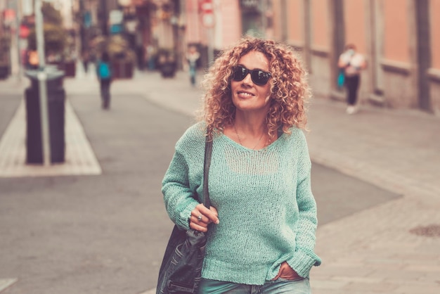 Smiling attractive female tourist walking in the street looking for shopping stores City tourism concept lifestyle One happy woman enjoying outdoor leisure activity in town centre wearing sunglasses