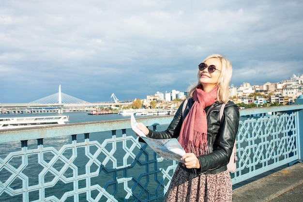 Smiling attractive tourist woman with map on Galata bridge in Istanbul Turkey Concept of travel and adventure