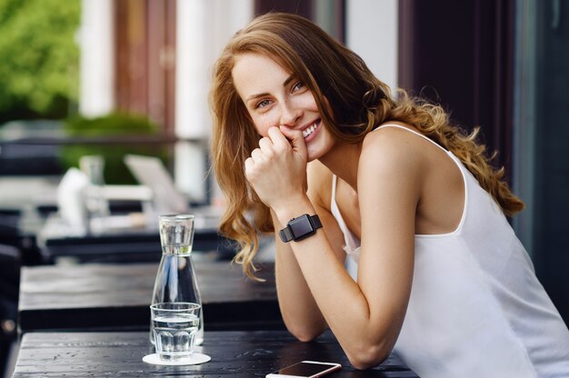 Smiling attractive woman sits in terrace and drinking water