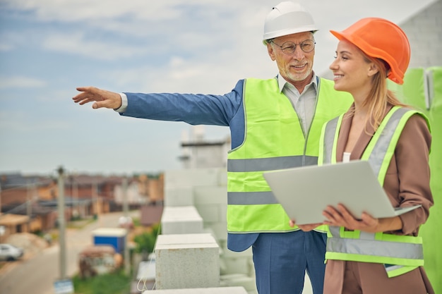 Photo smiling attractive young construction supervisor with a laptop in her hand listening to a foreman