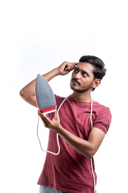 Smiling attractive young man househusband in apron hold in hands iron while doing housework isolated on yellow background studio portrait. Housekeeping concept.