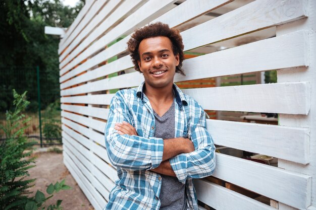 Smiling attractive young man in plaid shirt standing outdoors with arms crossed