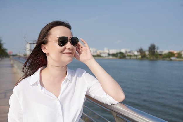 Smiling attractive young woman walking on river embarkment and looking at water