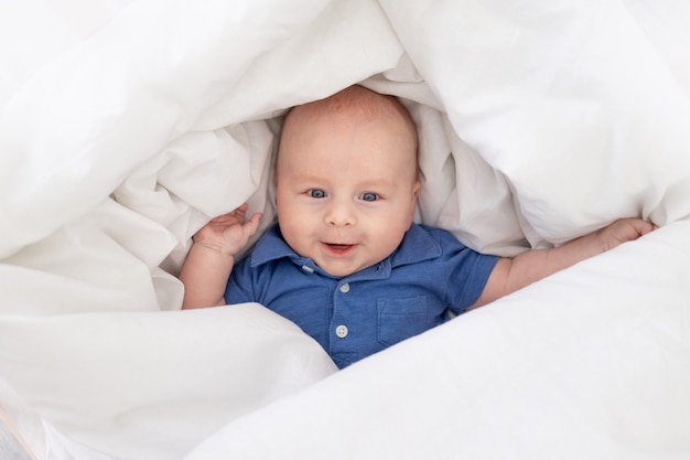 Smiling baby boy in a blanket in a crib, happy newborn woke up