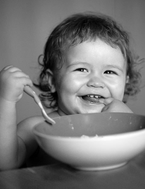 Bambino sorridente che mangia cibo bambino divertente che mangia cibo stesso con un cucchiaio sulla nutrizione sana della cucina fo