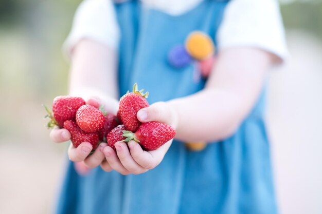 Smiling baby girl holding fresh strawberry outdoors