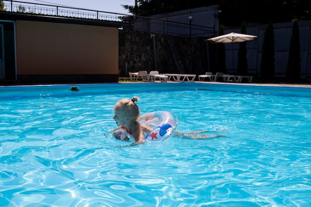 Smiling baby girl swims with an inflatable ring in a summer pool