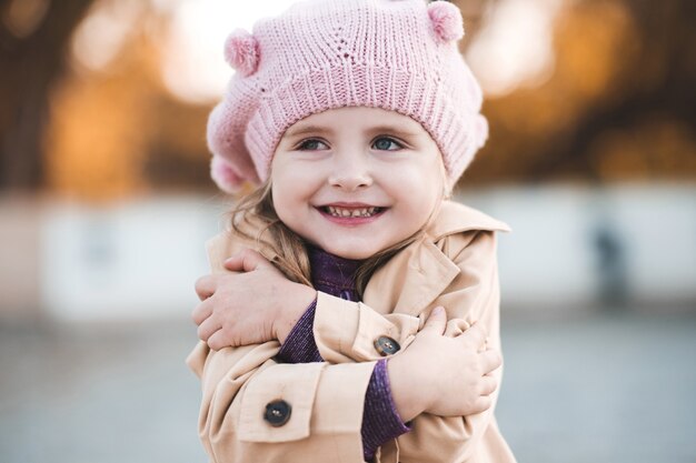 Smiling baby girl wearing knitted hat and jacket over autumn background