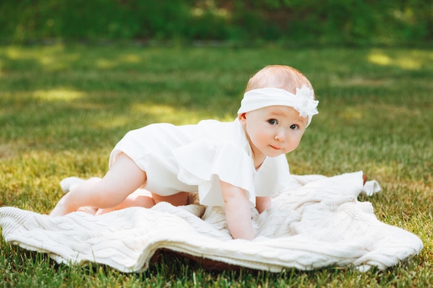 Smiling baby lies on a blanket on the grass in the park little girl 6 months old