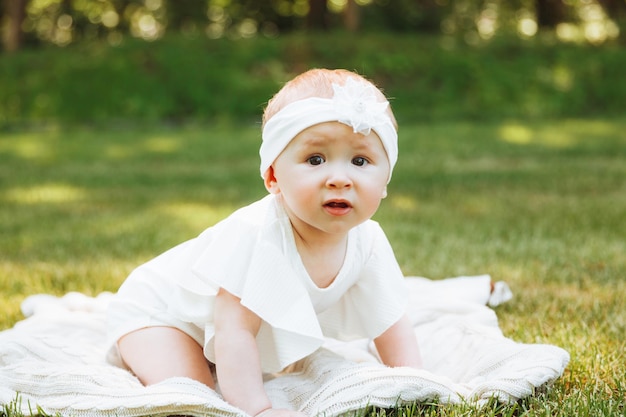 Smiling baby lies on a blanket on the grass in the park little girl 6 months old