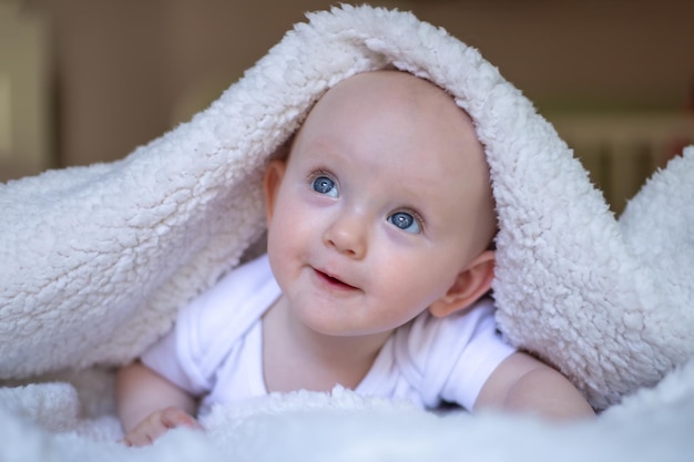 Smiling baby looking at camera under a white blanket towel