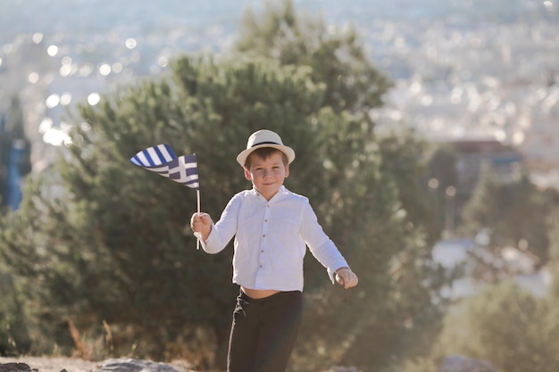 Smiling baby toddler boy holding a Greece flag on city background Independence Day Flag Day