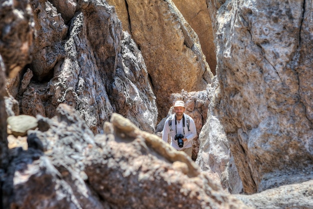 Smiling backpacker with camera goes down path between rocks, Hormuz Island, Hormozgan,  Iran.