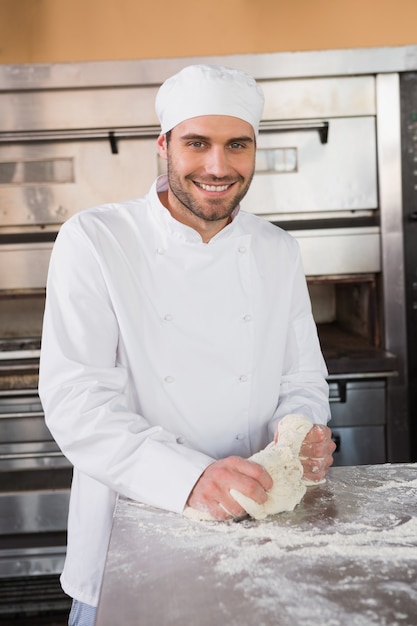 Smiling baker kneading dough at counter