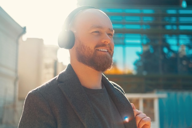 Smiling bald bearded man enjoys his headphones while walking in sunlight