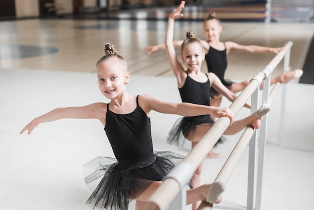 Smiling ballerina girls stretching their legs on barre