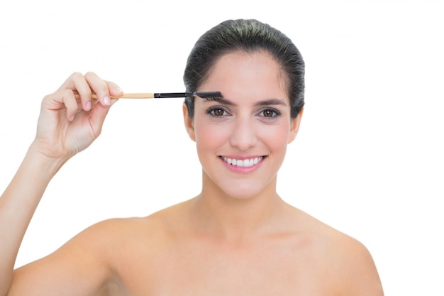 Smiling bare brunette using eyebrow brush