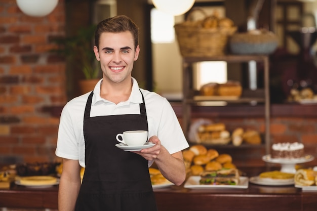 Smiling barista holding cup of coffee