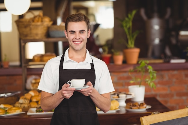 Smiling barista holding cup of coffee