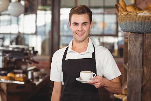 Smiling barista offering cup of coffee to camera