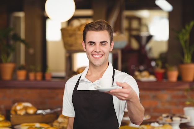 Smiling barista offering cup of coffee to camera