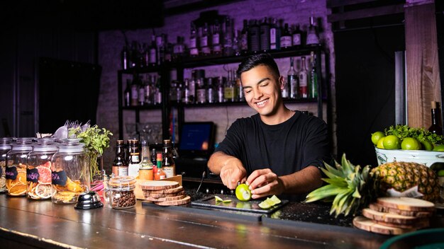 Smiling bartender behind a club bar cutting lime into pieces