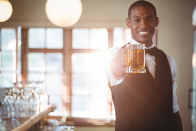 Smiling bartender offering a glass of beer at bar counter