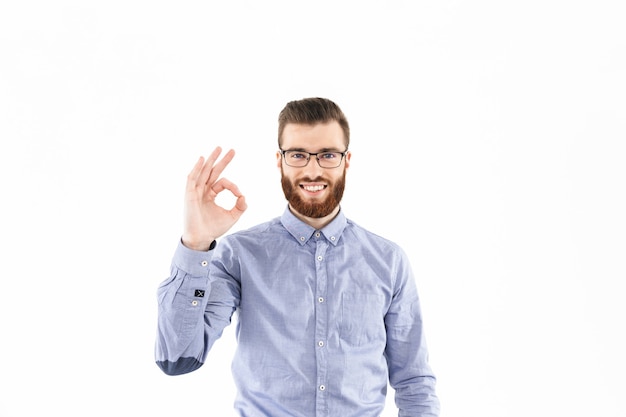 Smiling bearded elegant man in eyeglasses showing ok sign and looking