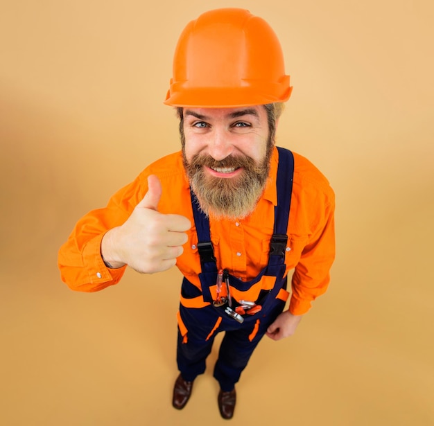 사진 작업복과 안전모를 쓴 웃는 수염난 남자가 안전모와 유니폼을 입은 엄지손가락 건축업자를 보여주고 있습니다.