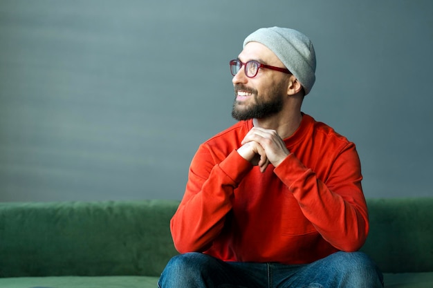 Smiling bearded man wearing stylish eyeglasses and hipster hat looking away planning startup