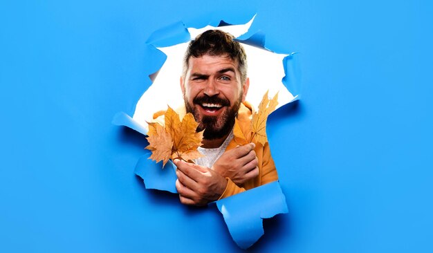 Smiling bearded man with autumn leaves looking through paper fashion trends for fall autumn fashion