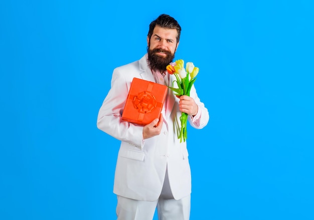 Smiling bearded man with present box and bouquet of flowers businessman in suit with gift and