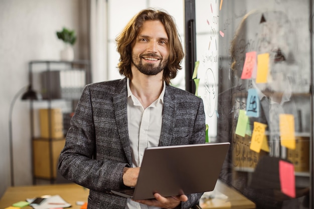 Foto manager barbuto sorridente che lavora con il computer portatile in un ufficio moderno