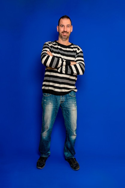 Smiling bearded spanish man poses with arms crossed in full length vertical photo isolated on blue studio background person