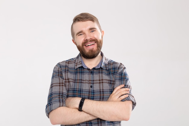 Smiling bearded young man rejoices coming weekends, dressed casually, over white wall