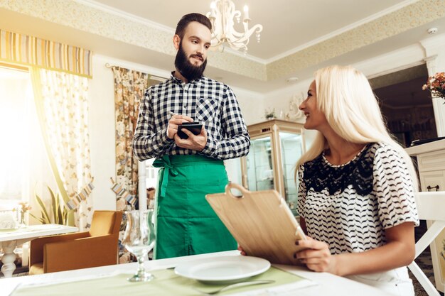 Smiling bearded young waiter taking order in cafe