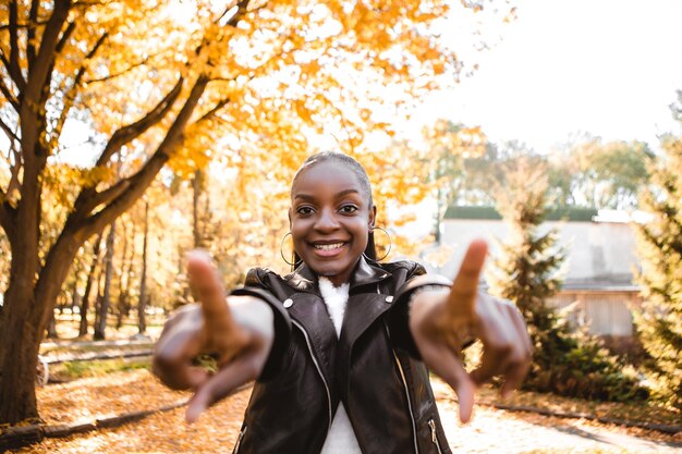 写真 秋の都市公園の外に立っている指のシンボルを指している笑顔の美しいアフリカの女性