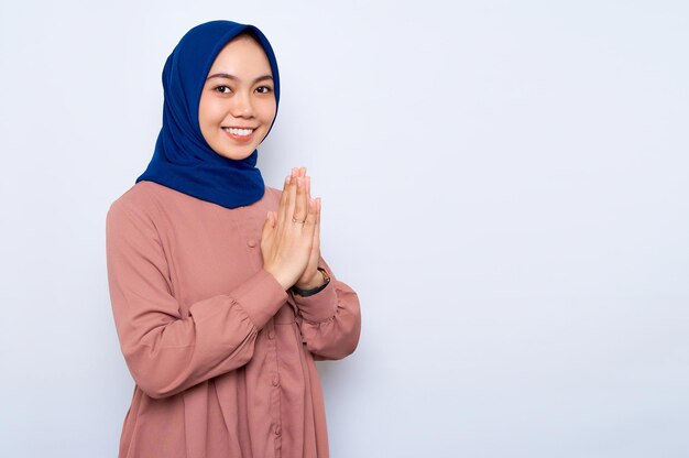 Smiling beautiful Asian muslim woman in casual shirt gesturing eid mubarak greeting isolated over white background People religious lifestyle concept