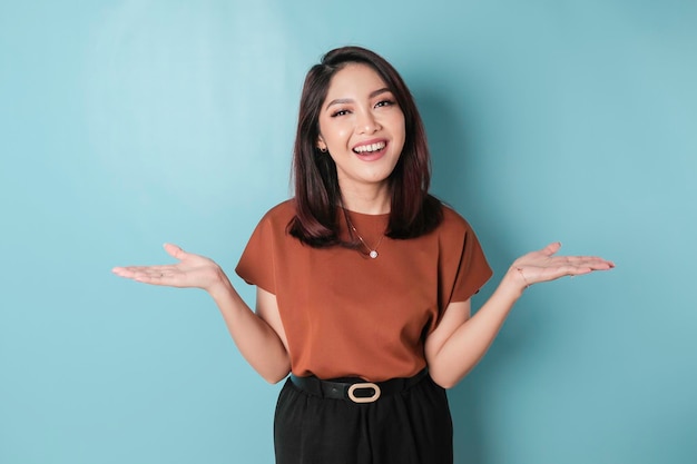 Smiling beautiful Asian woman pointing finger sideward to empty space isolated blue background