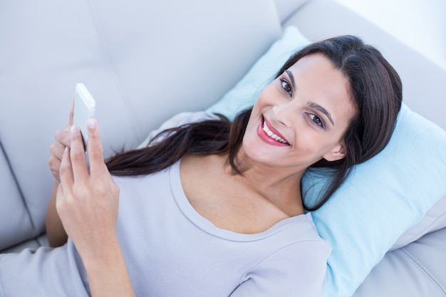 Smiling beautiful brunette relaxing on the couch and using her phone