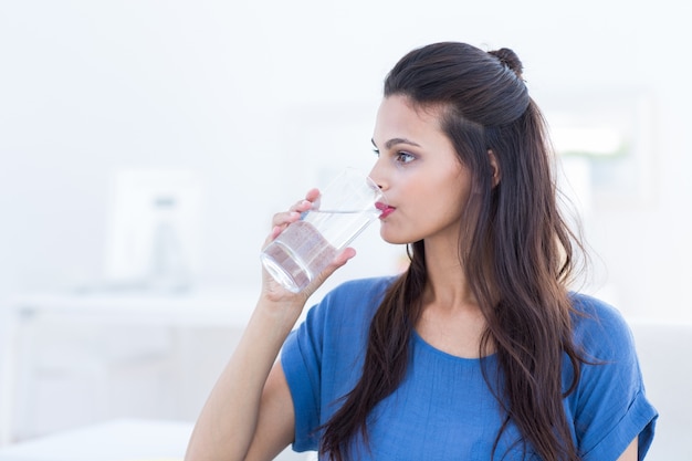 Smiling beautiful brunette sitting on the couch and drinking water