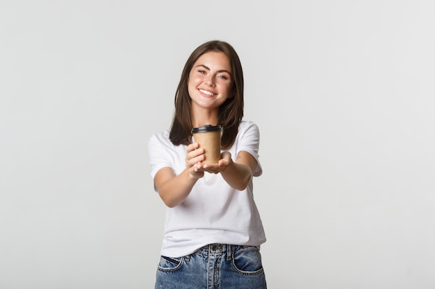 Smiling beautiful brunette woman giving you cup of coffee.