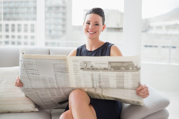 Smiling beautiful businesswoman reading newspaper on sofa