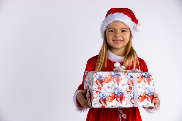 Smiling beautiful caucasian girl in Santa red hat and costume holding Christmas gift in hand