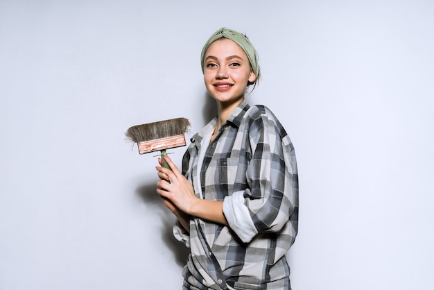 Smiling beautiful girl doing repairs in her apartment, holding brush for painting walls