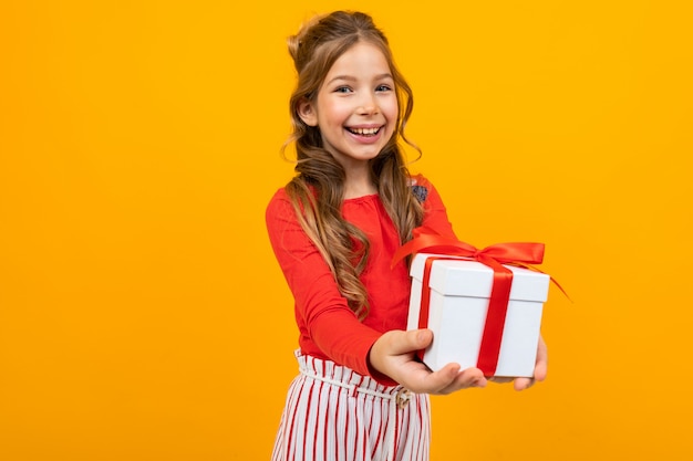 Улыбающаяся красивая девушка протягивает коробку с подарком на день рождения на желтом