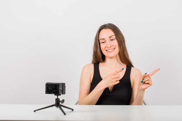 Smiling beautiful girl is posing at camera by pointing right with forefingers on white background