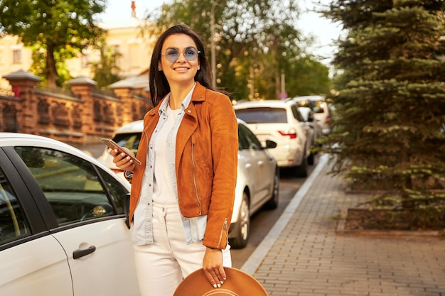 Smiling beautiful lady in sunglasses using smartphone outdoor