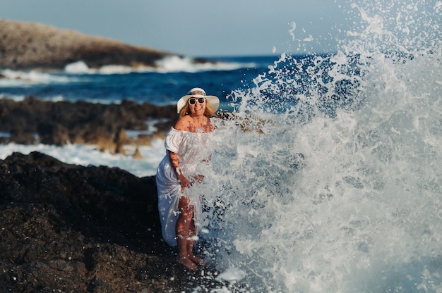 Sorridente bella donna sulla spiaggia in un cappello di paglia sull'isola di zakynthos.a ragazza in un abito bianco al tramonto sull'isola di zante, grecia.